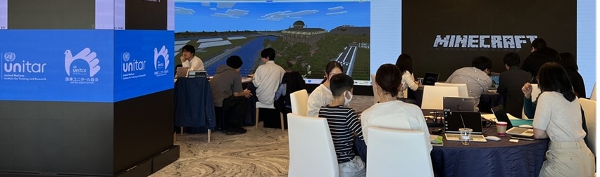 Several people seated in a room, focused on a speaker presenting information on a screen.