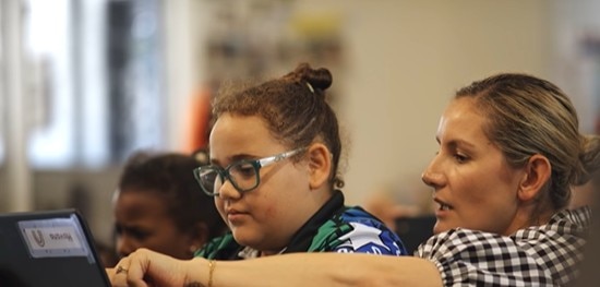 Teacher helps a student use a laptop in the classroom.