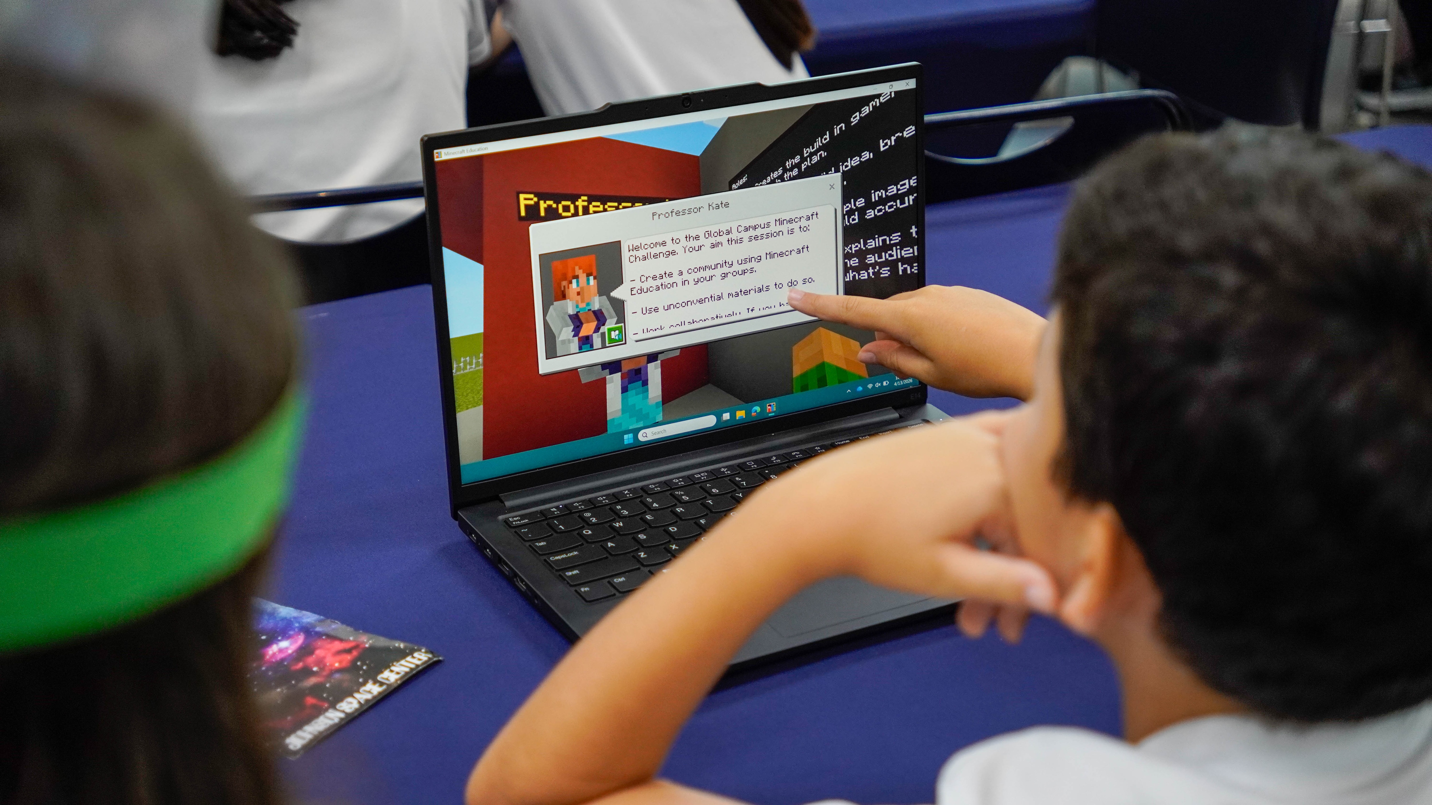 Student points at a laptop screen showing a Minecraft challenge prompt.
