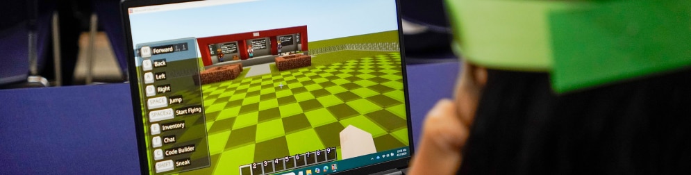 Student looks at a laptop showing a Minecraft screen with movement controls and a code builder option.