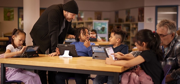 Four young students are using tablet computers. Two instructors are assisting them.