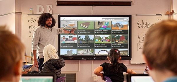 A teacher presents Minecraft lessons on a screen to a classroom of students.
