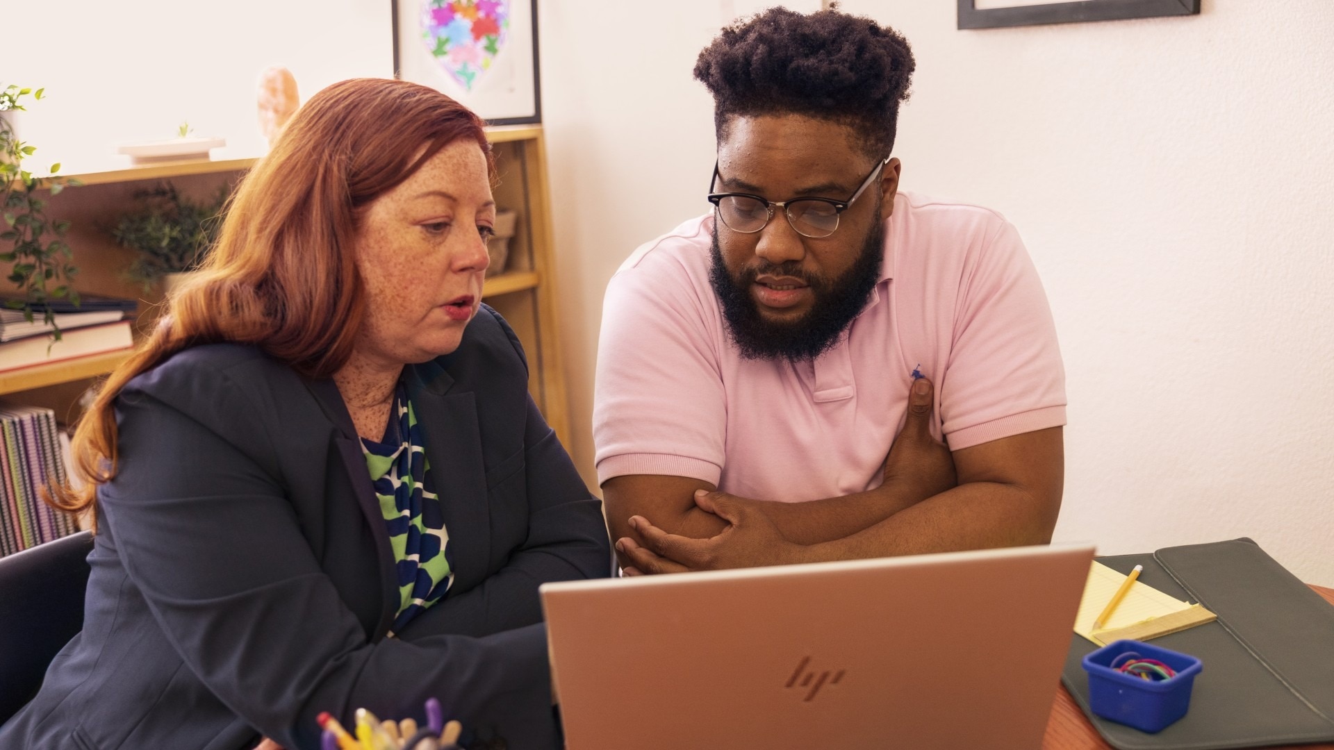 A woman and a man look at a laptop in an office.