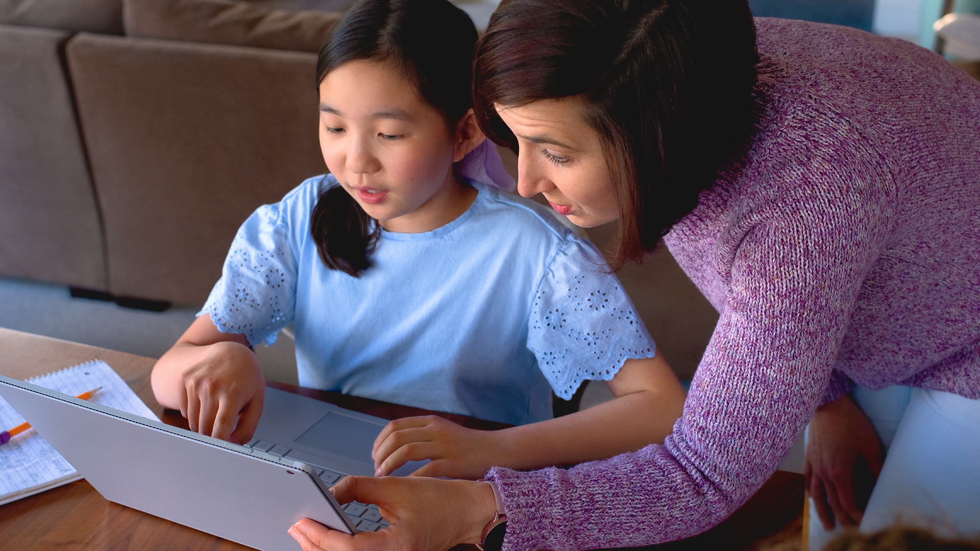 A woman helps a young girl use a laptop.