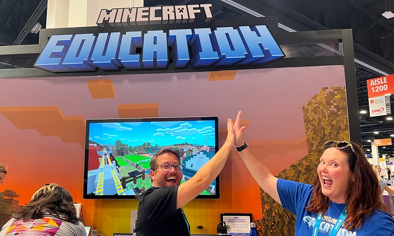 Two people high-fiving in front of a Minecraft Education booth.