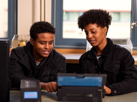Two people using a tablet device together in a room with a window in the background.